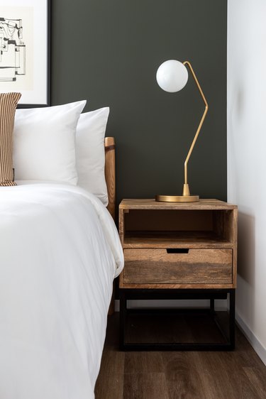 Modern bedroom with rustic nightstand, gray wall, brass lamp.